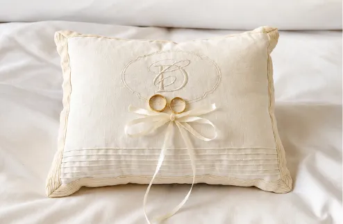 Almohada de anillos de lino marfil con monograma bordado, alforzas y dos aros de oro sobre lazo de satín